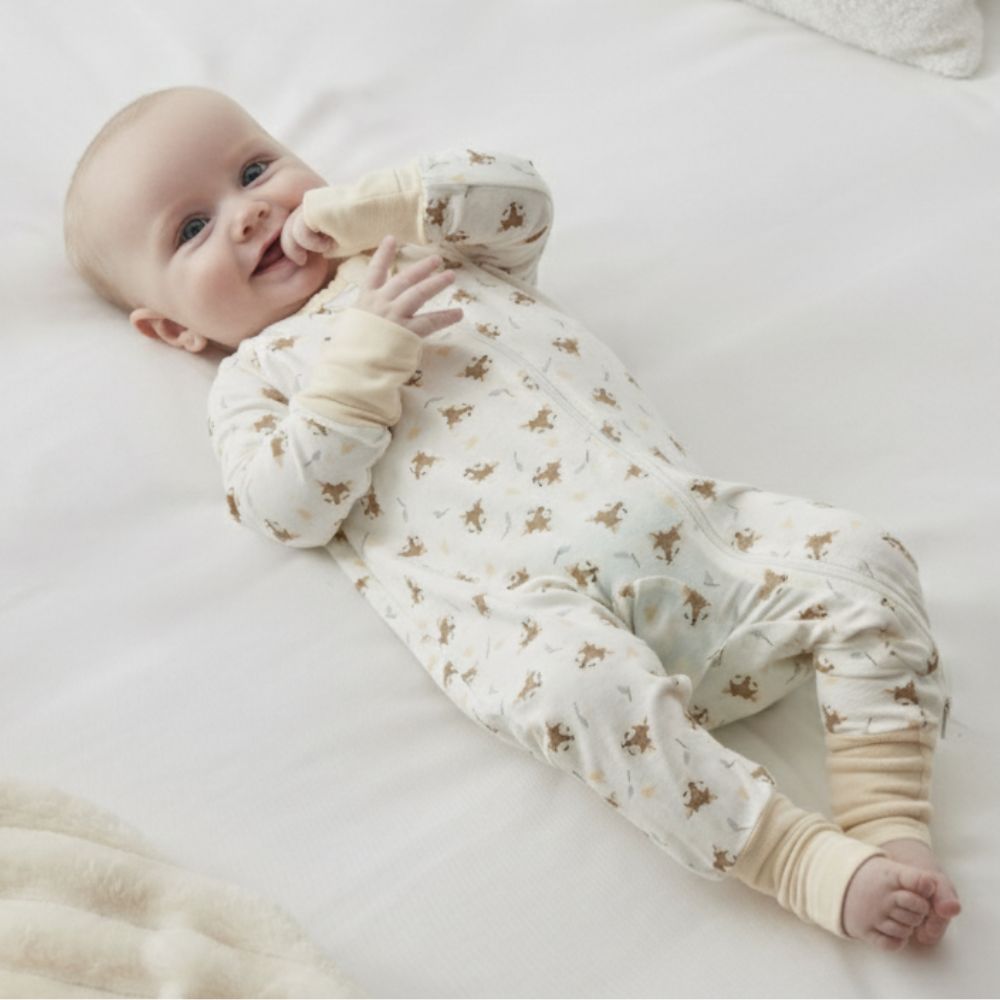 A baby lying on a white surface, wearing Zelkii's long-sleeve fawn-print bamboo pyjamas.