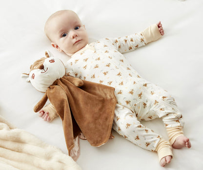A baby in Zelkii's fawn-print pyjamas lies next to the 'awake' Zelkii fawn LuviDuvi lovey.