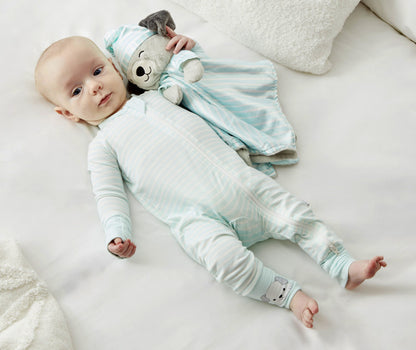 A baby lies on a white surface, wearing Zelkii's blue and white striped puppy pyjamas and holding the matching 'asleep' puppy LuviDuvi lovey.