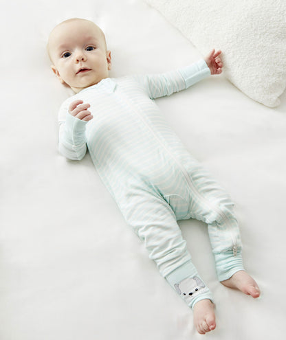 A baby lying on a white surface, wearing Zelkii's blue and white striped pyjamas with a puppy on the ankle cuff.