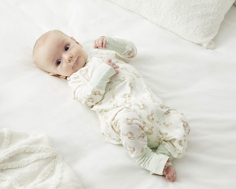 Lifestyle image of a baby wearing the Zelkii bunny-print pyjamas with mint green cuffs.