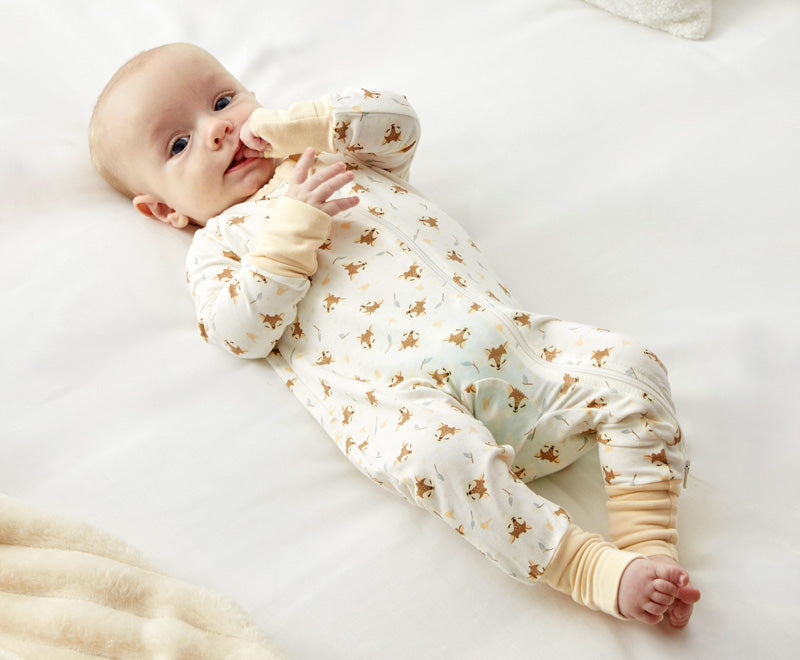 A baby lying on a white surface, wearing Zelkii's long-sleeve fawn-print bamboo pyjamas.