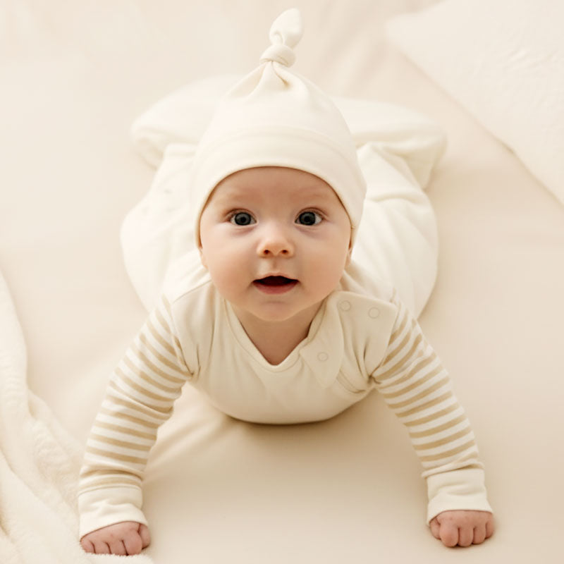 Lifestyle image of a baby wearing the Zelkii cream knotted beanie.