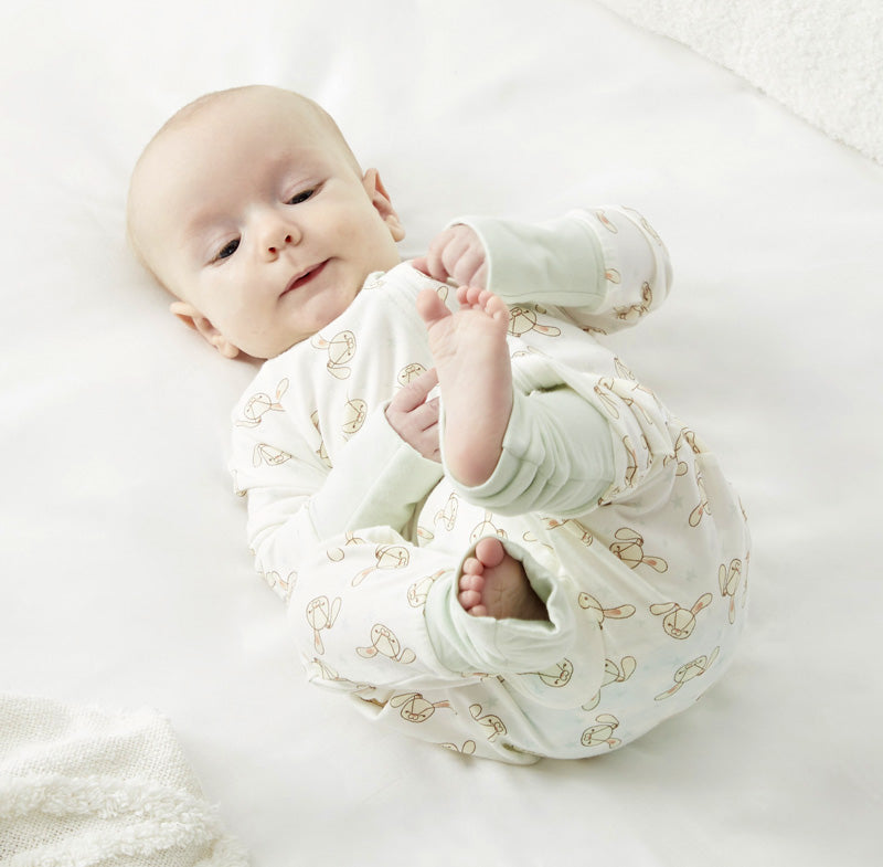 A baby in Zelkii's bunny-print pyjamas, lying on its back and looking up.