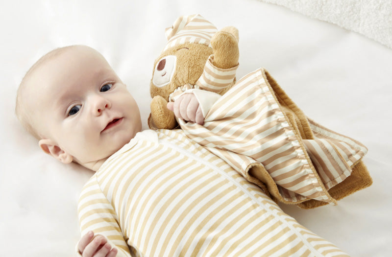 Lifestyle image of a baby in zelkii  striped teddy bear pyjamas, holding the 'asleep' Zelkii teddy bear LuviDuvi lovey.