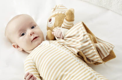 Lifestyle image of a baby in zelkii  striped teddy bear pyjamas, holding the 'asleep' Zelkii teddy bear LuviDuvi lovey.