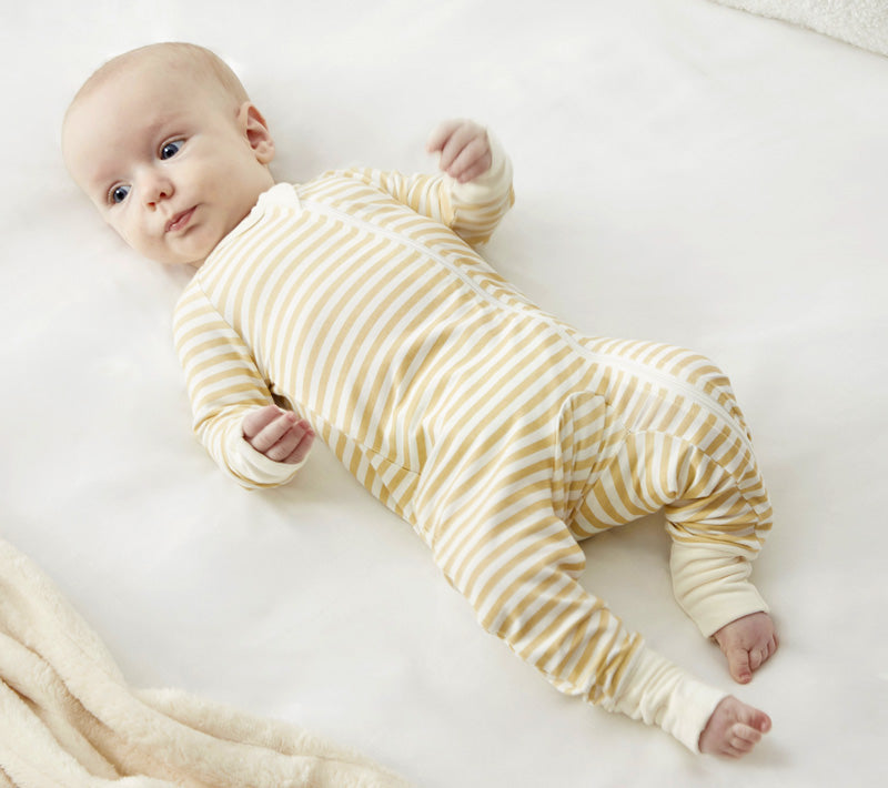 A baby lying on a white surface, wearing Zelkii's teddy bear  yellow and cream striped bamboo pyjamas.